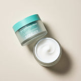 Skincare cream jar with lid off on a textured teal background